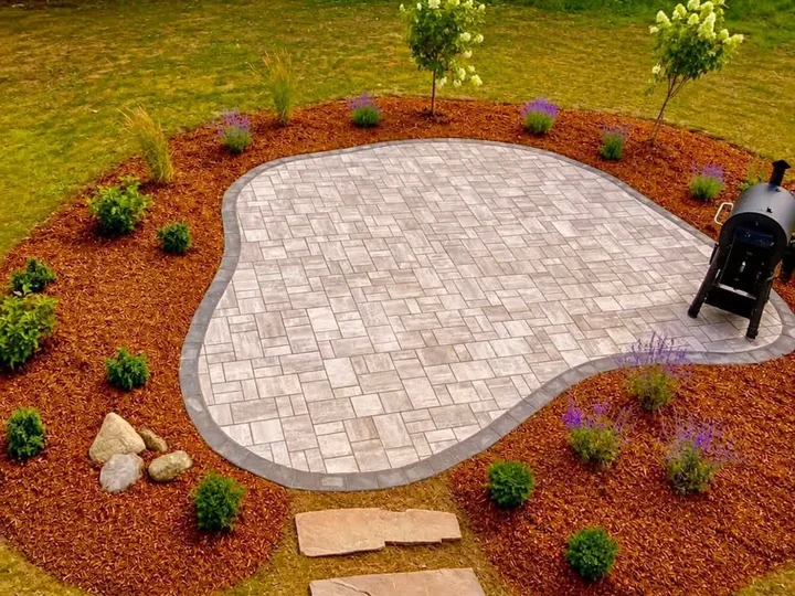 Rounded paver patio with a charcoal border, new plantings in mulch and a stepping stone path