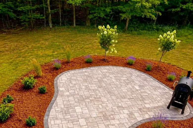 Rounded paver patio with a charcoal border and new plantings in mulch, built by Up North Scapes