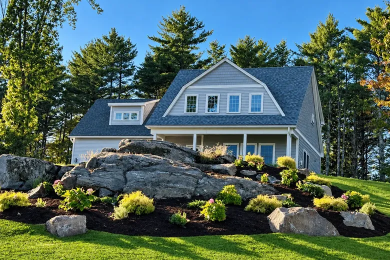 Boulders and new plantings around a natural rock ledge in front of a gray house