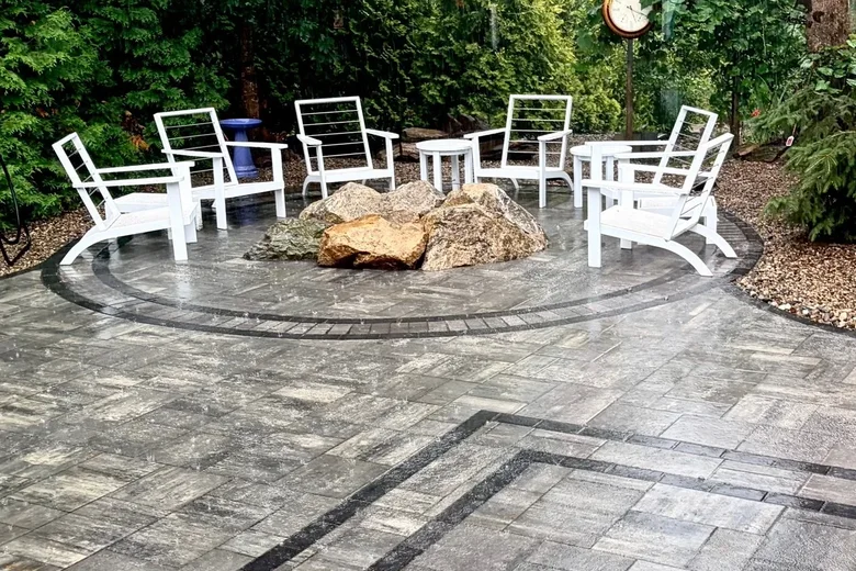 Paver patio with a circular inlay and a boulder fire feature at the center, built by Up North Scapes