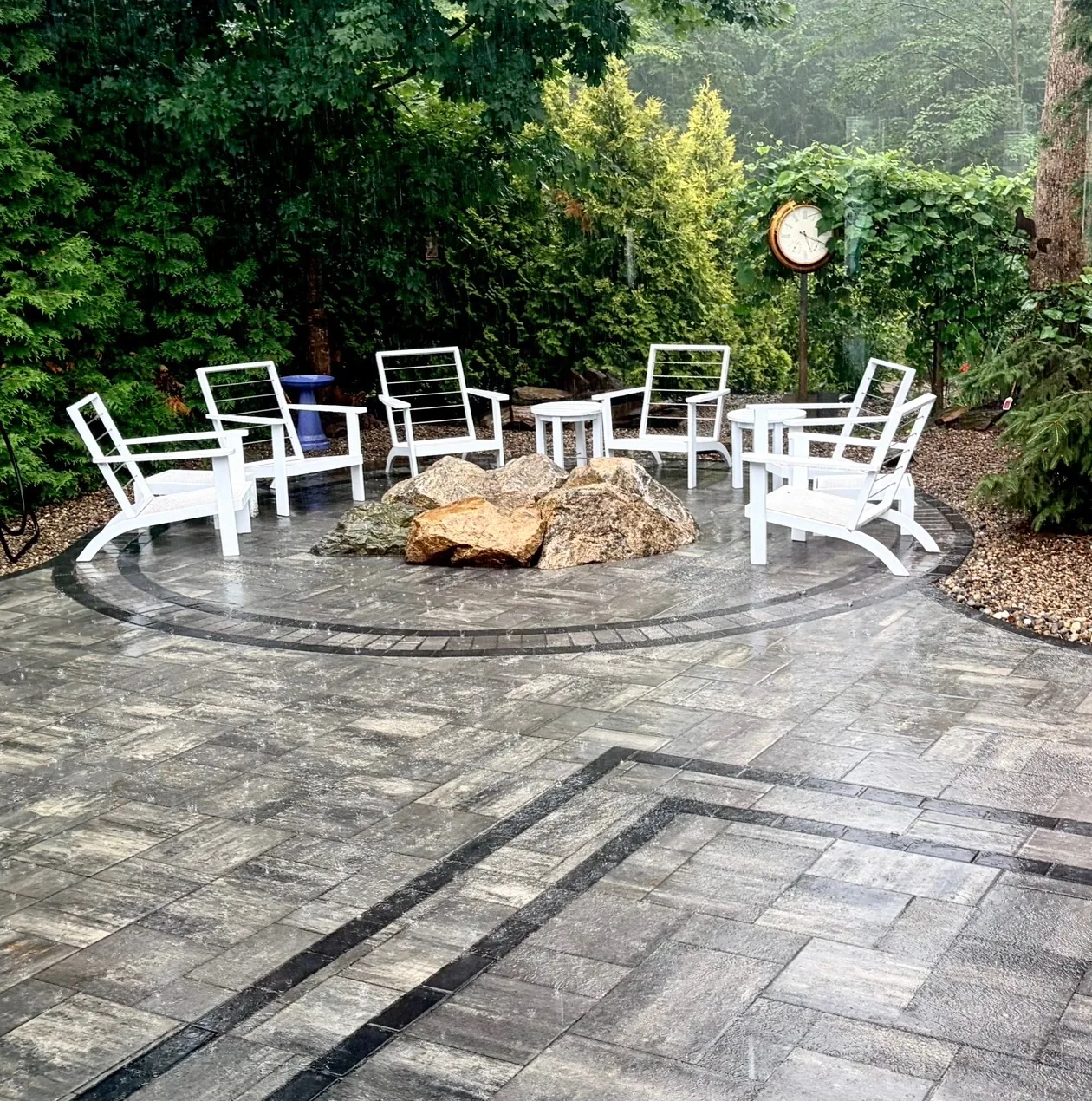Backyard design with circular paver patio, natural boulder fire pit surround, and Adirondack-style seating - Up North Scapes NH