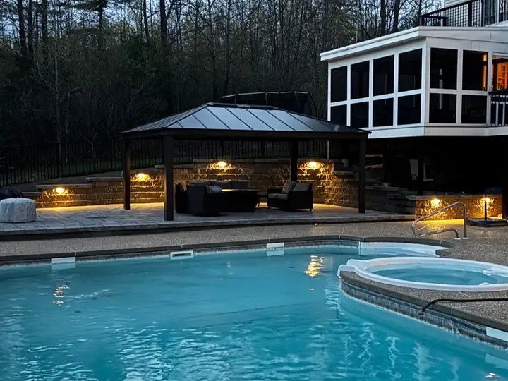 Poolside patio at dusk with a pavilion, lit stone walls and seating