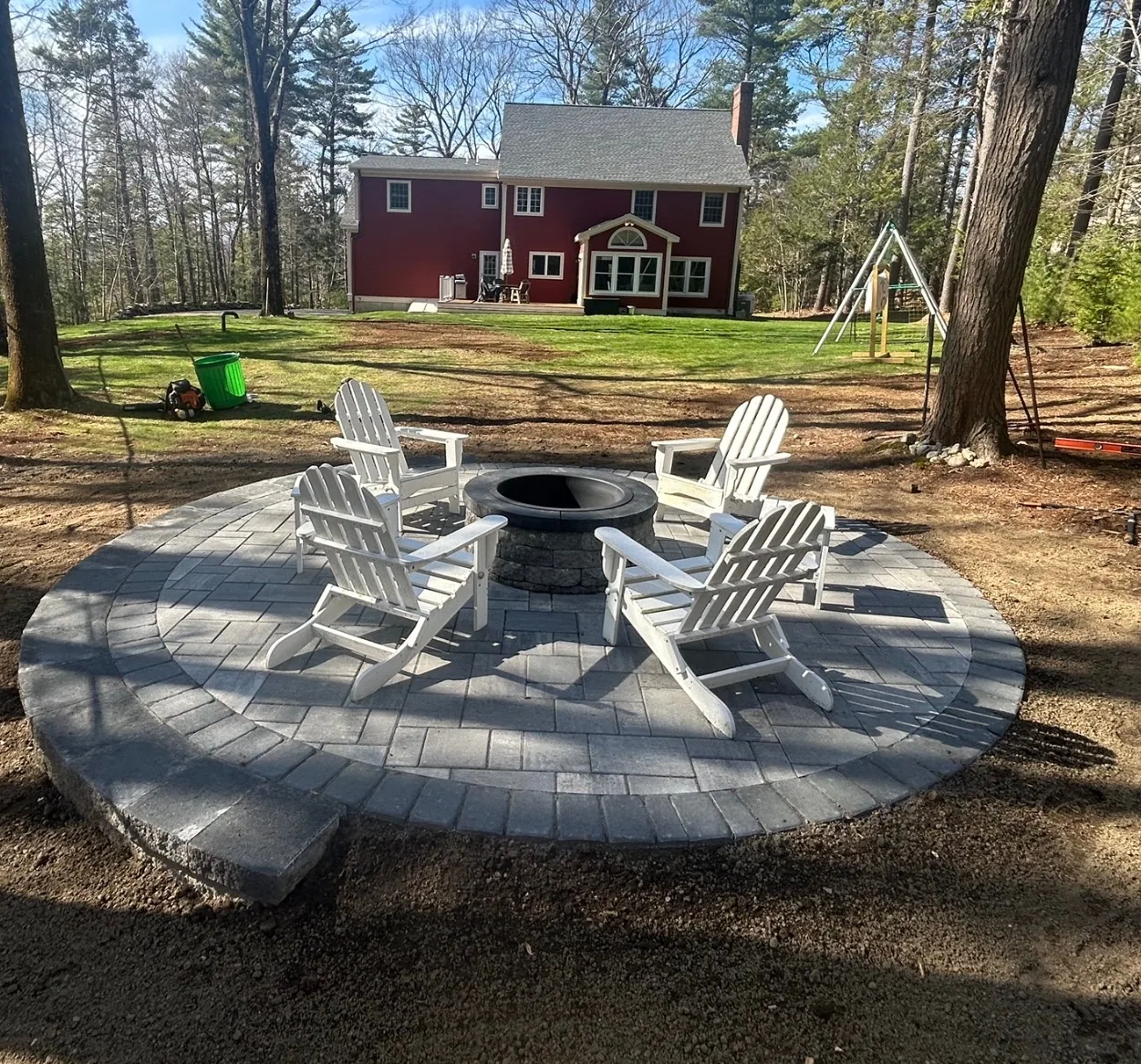 Backyard design with circular paver patio, fire pit, and white Adirondack chairs - Up North Scapes NH
