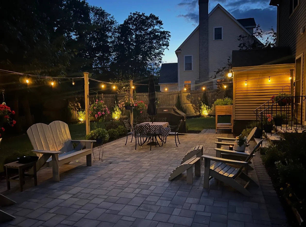 Paver patio under string lights at twilight by Up North Scapes