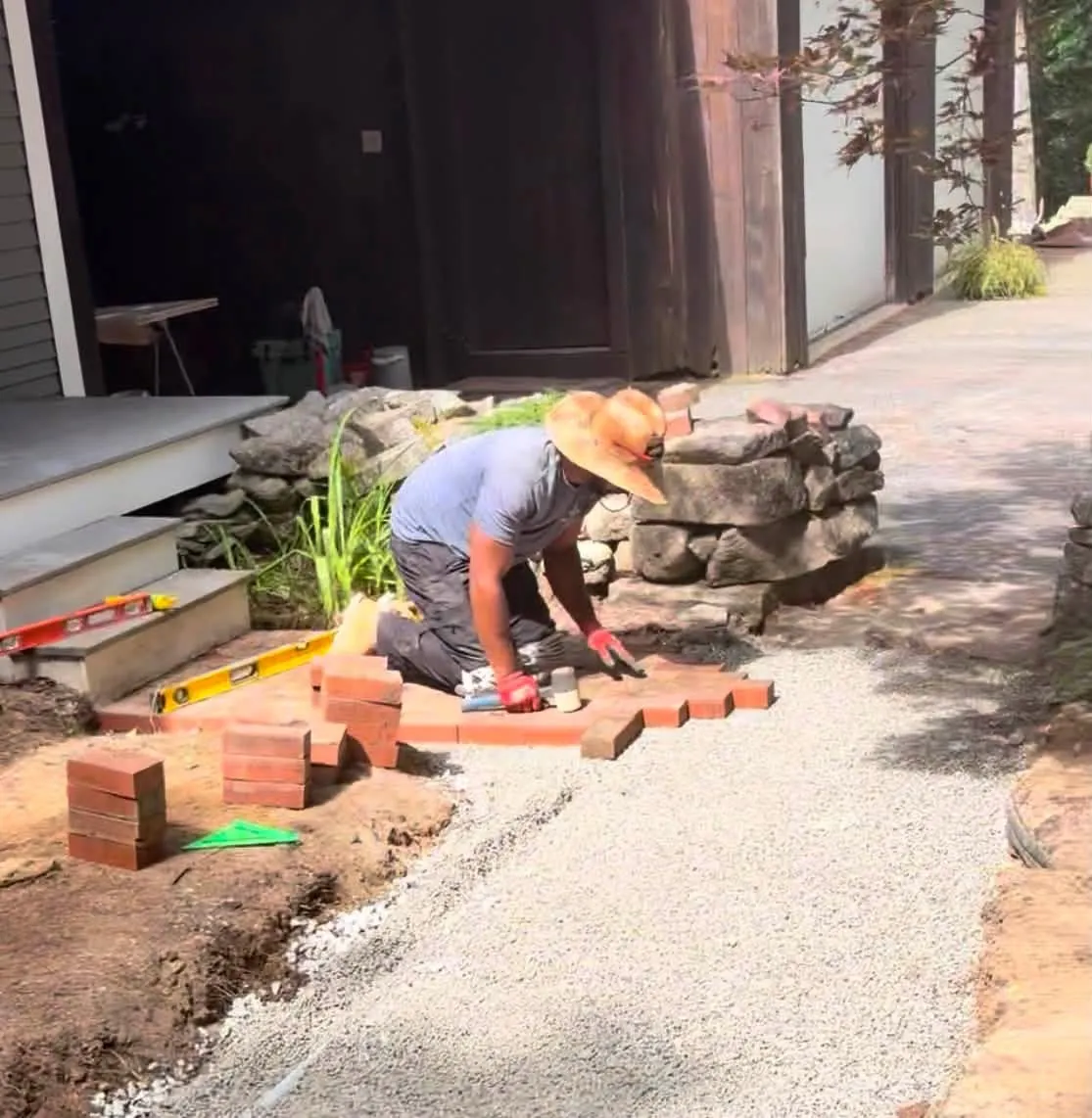 Brick being set on a gravel bed beside an old fieldstone wall