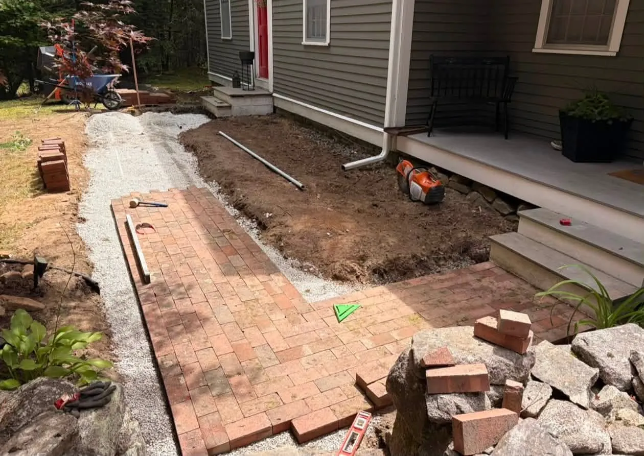 A brick walk half laid on its gravel bed beside a house