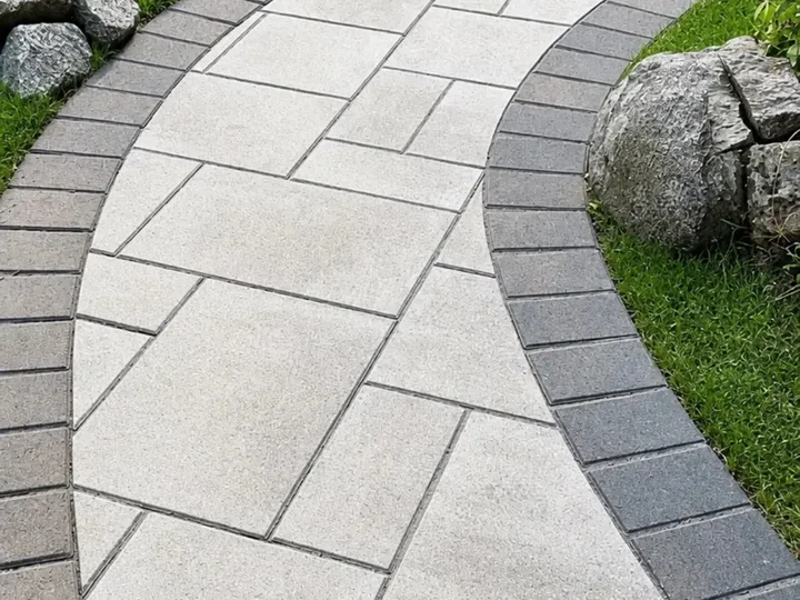 Curved light paver walkway with a charcoal border beside a boulder