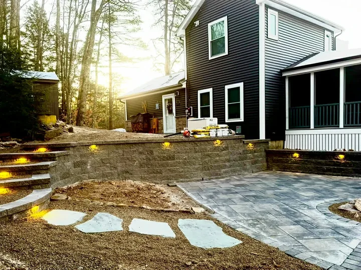 Block retaining wall with lit steps, stone steppers and a paver patio behind a house