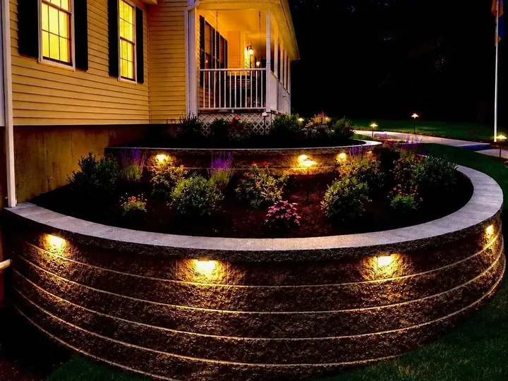 Curved block planter wall lit under the cap beside a porch at night