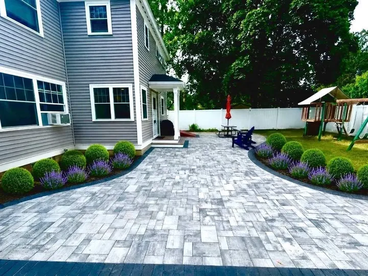 Wide paver patio along the side of a house with planting beds on both edges