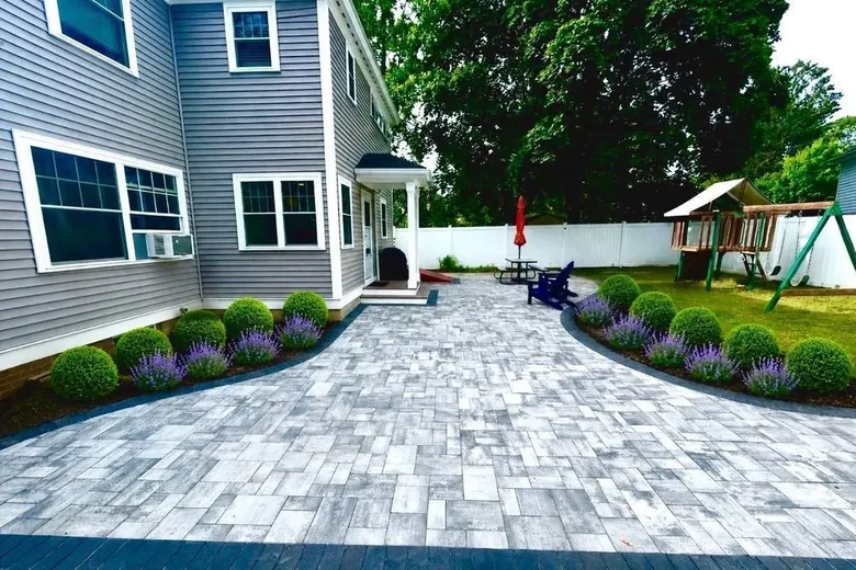 Wide paver patio along the side of a house with planting beds on both edges, built by Up North Scapes