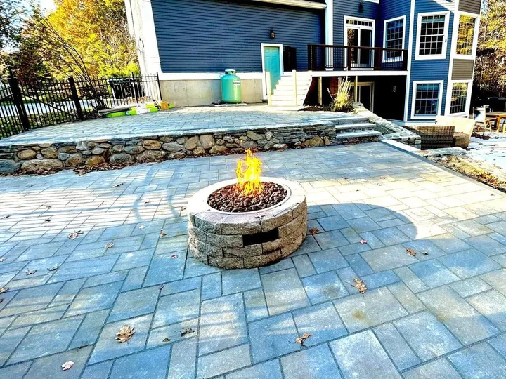 Paver patio with a fire pit and a stone faced wall behind a blue house