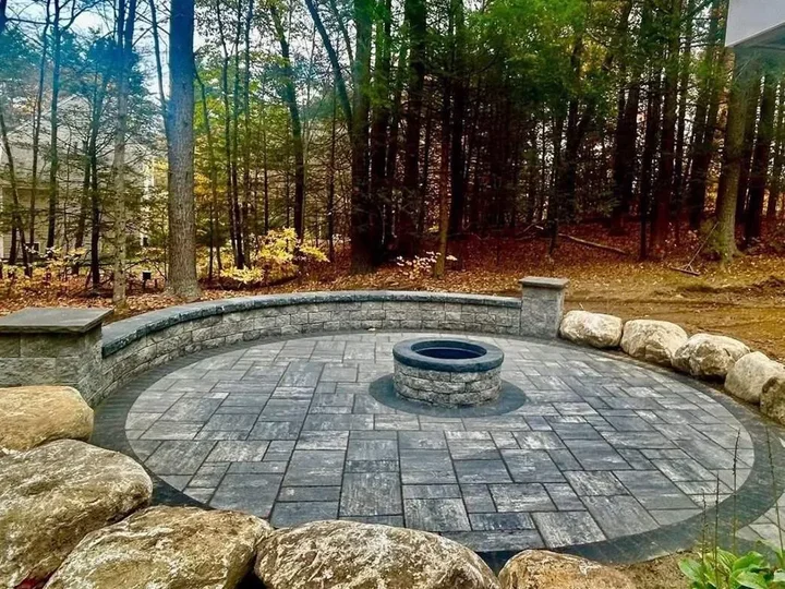 Round paver patio with a seating wall and fire pit, ringed by large boulders