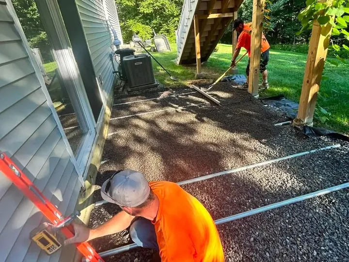 Crew member checking the grade on a gravel base before pavers
