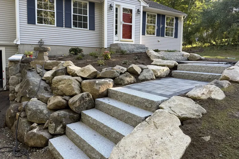 New perennials set among boulders beside granite steps up to a house
