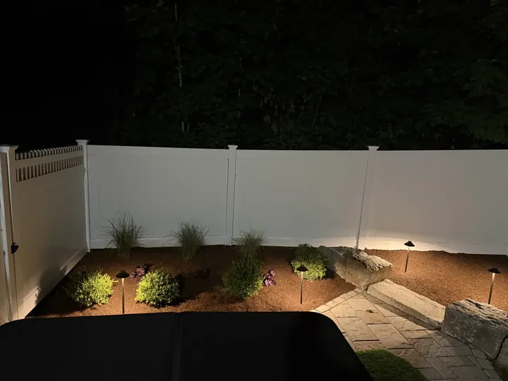 New planting bed with path lights along a vinyl fence at night