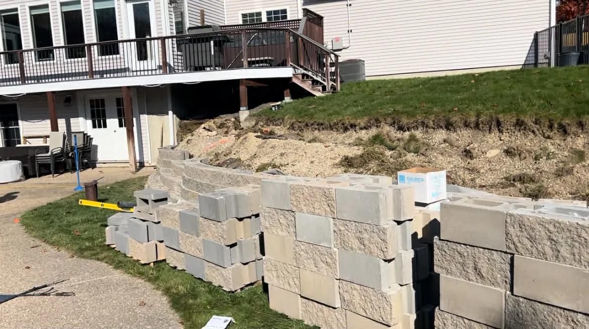 New retaining wall block being laid in curved courses below a backyard slope