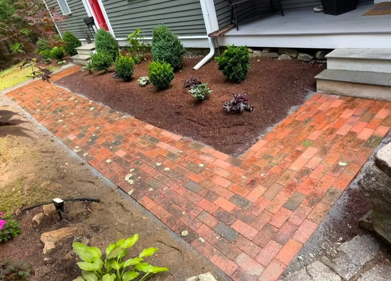 A short red brick walk turning the corner beside a planting bed