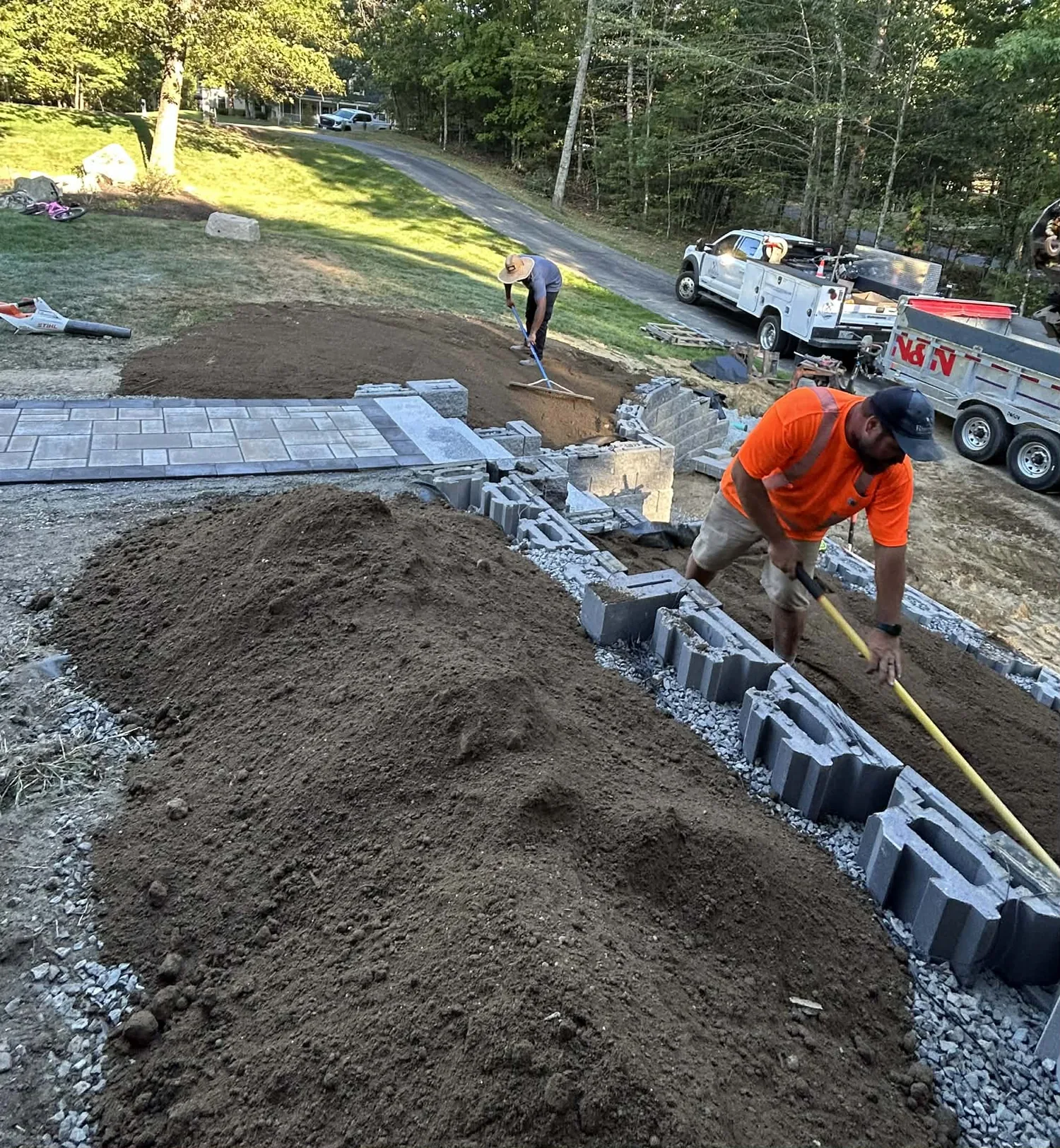 Worker setting the first courses of a block wall with stone and soil behind it