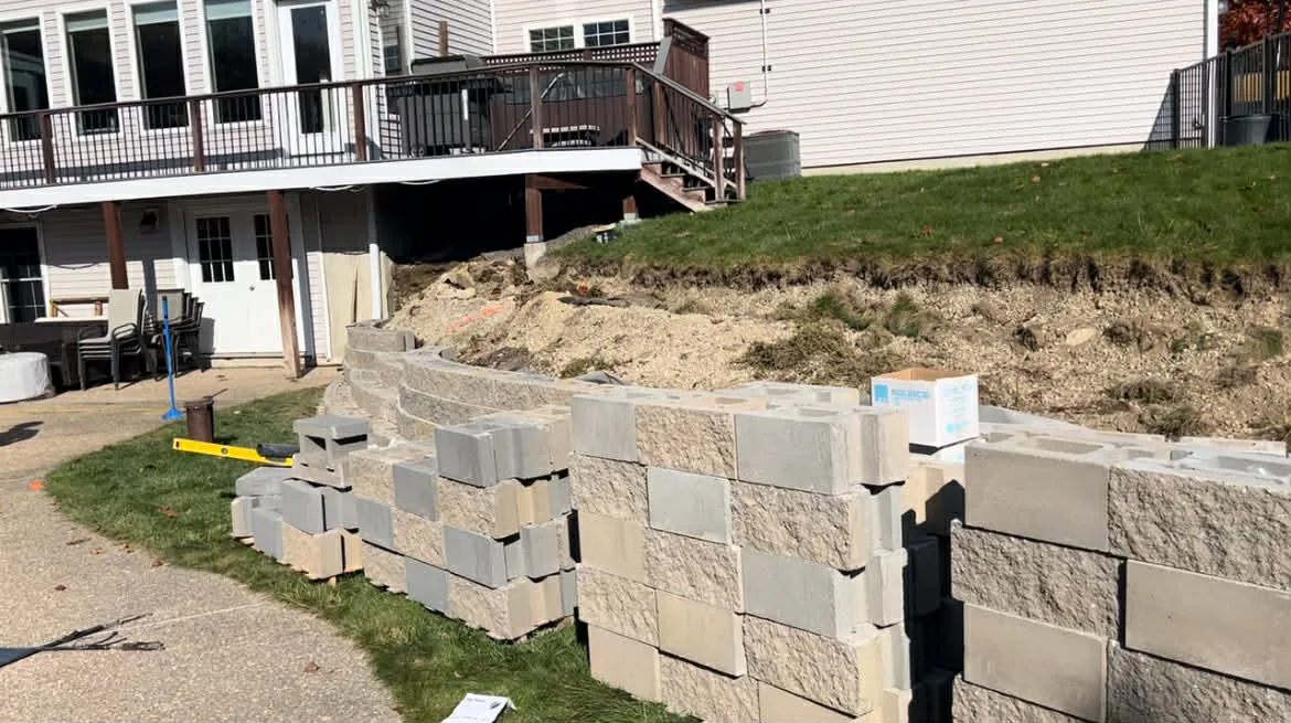 Block retaining wall partway up behind a house, with soil still to be backfilled